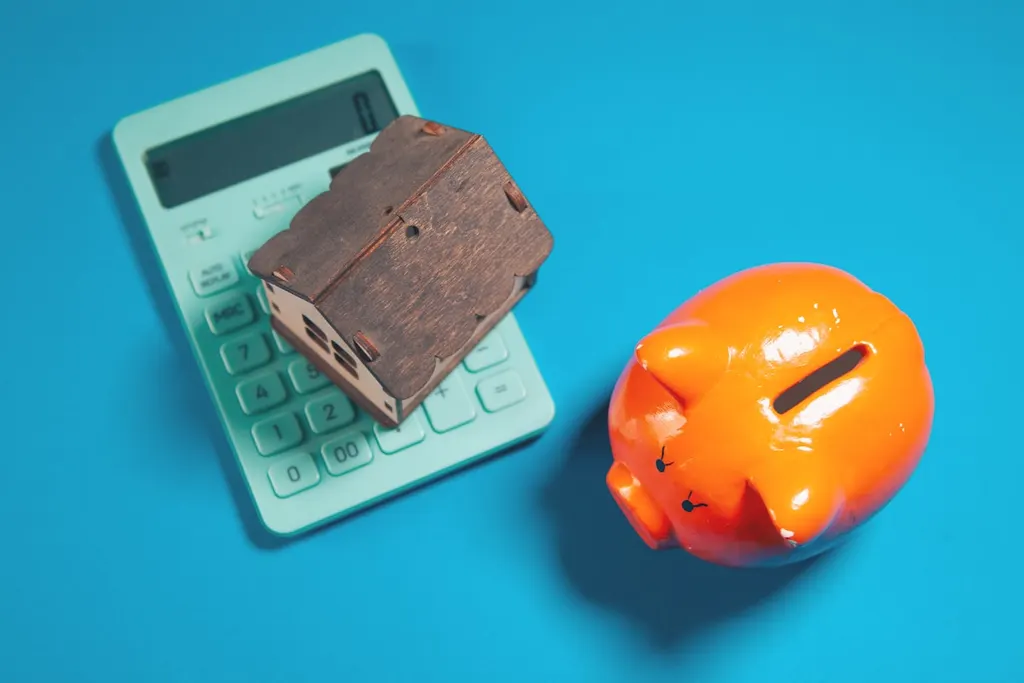 A calculator, a piggy bank and a model house on a blue ground.